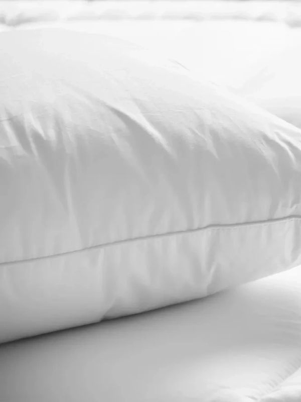 Close-up of a white pillow on a white bedspread.