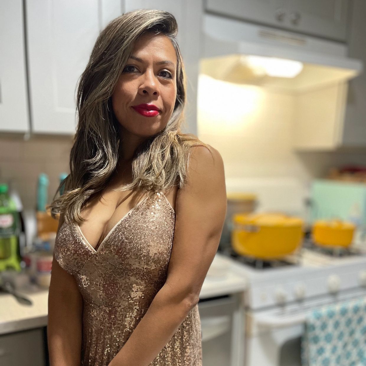 Woman in a sparkling dress posing in a kitchen.