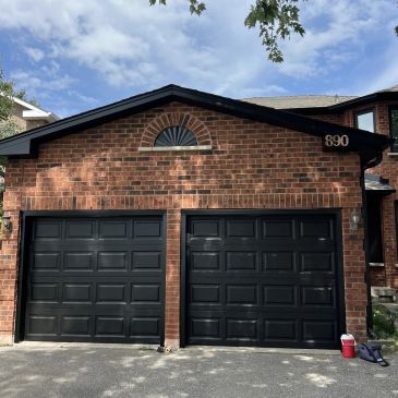 Brick house with two black garage doors under a partly cloudy sky.