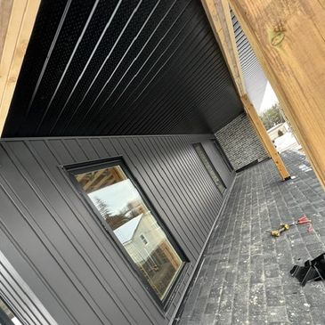 Newly constructed porch with black siding and wooden beams.