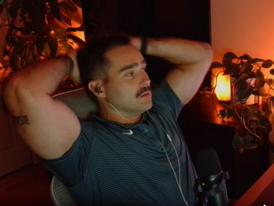 Man relaxing with hands behind head in a dimly lit room.