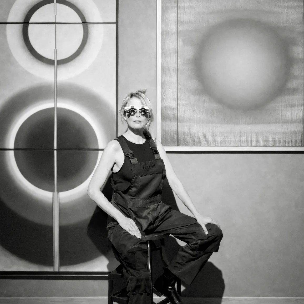 Pi Square artist seated in studio with geometric paintings exploring light, structure and perception
