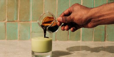Pouring espresso into a glass of green matcha latte with a spoon on the side.