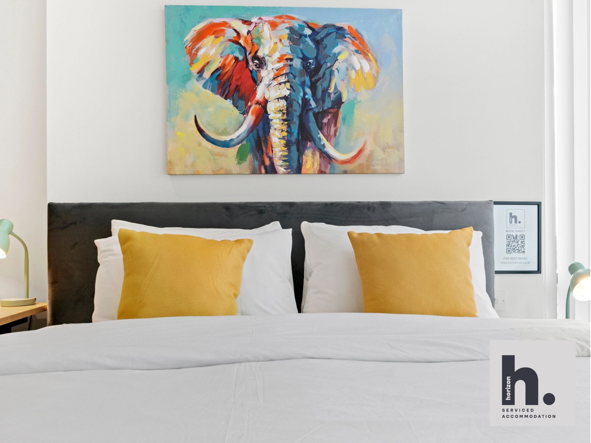 Colorful elephant painting above a neatly made bed with yellow pillows.