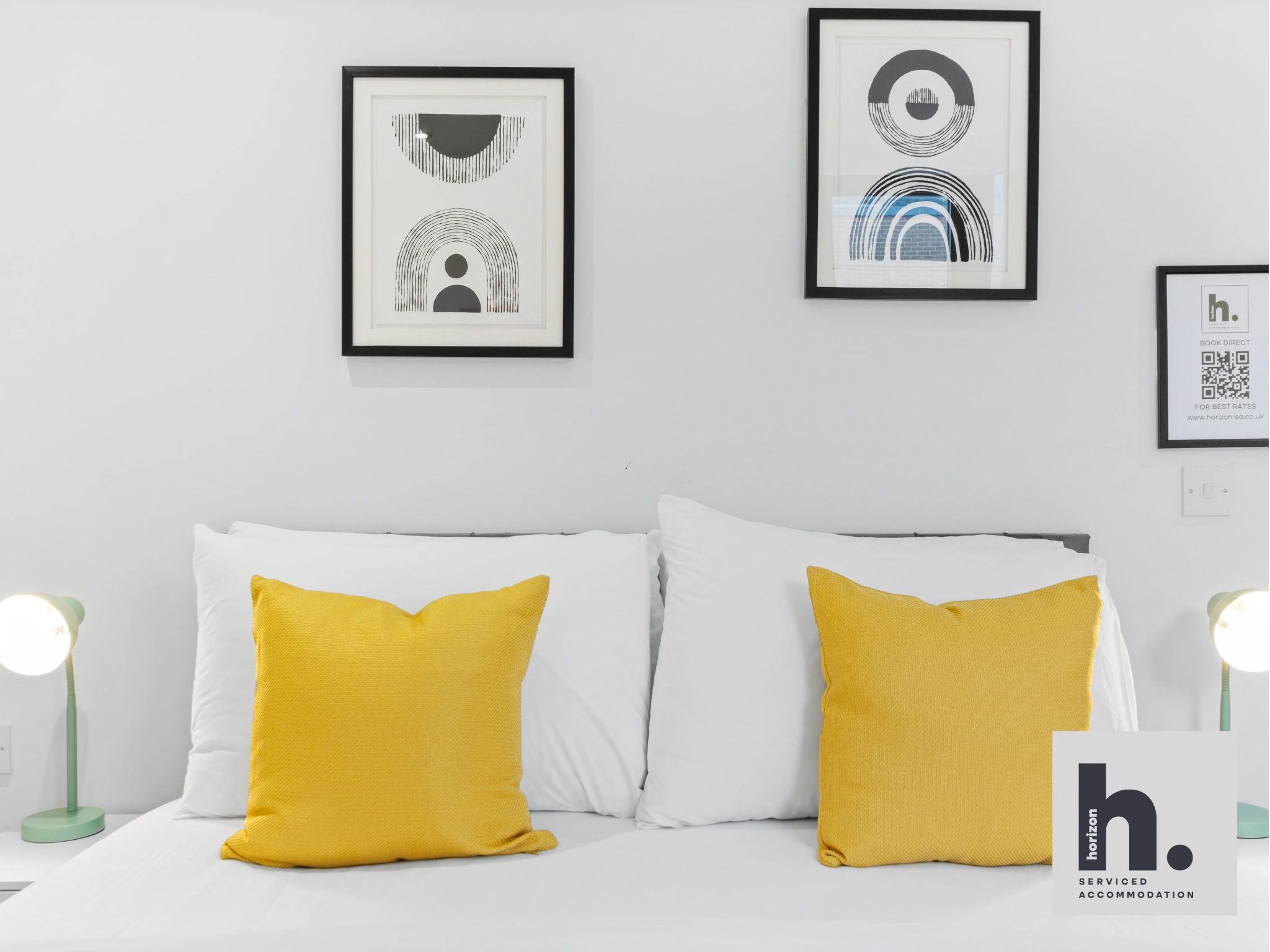 Modern bedroom with white bedding and yellow pillows beneath abstract black-and-white art.