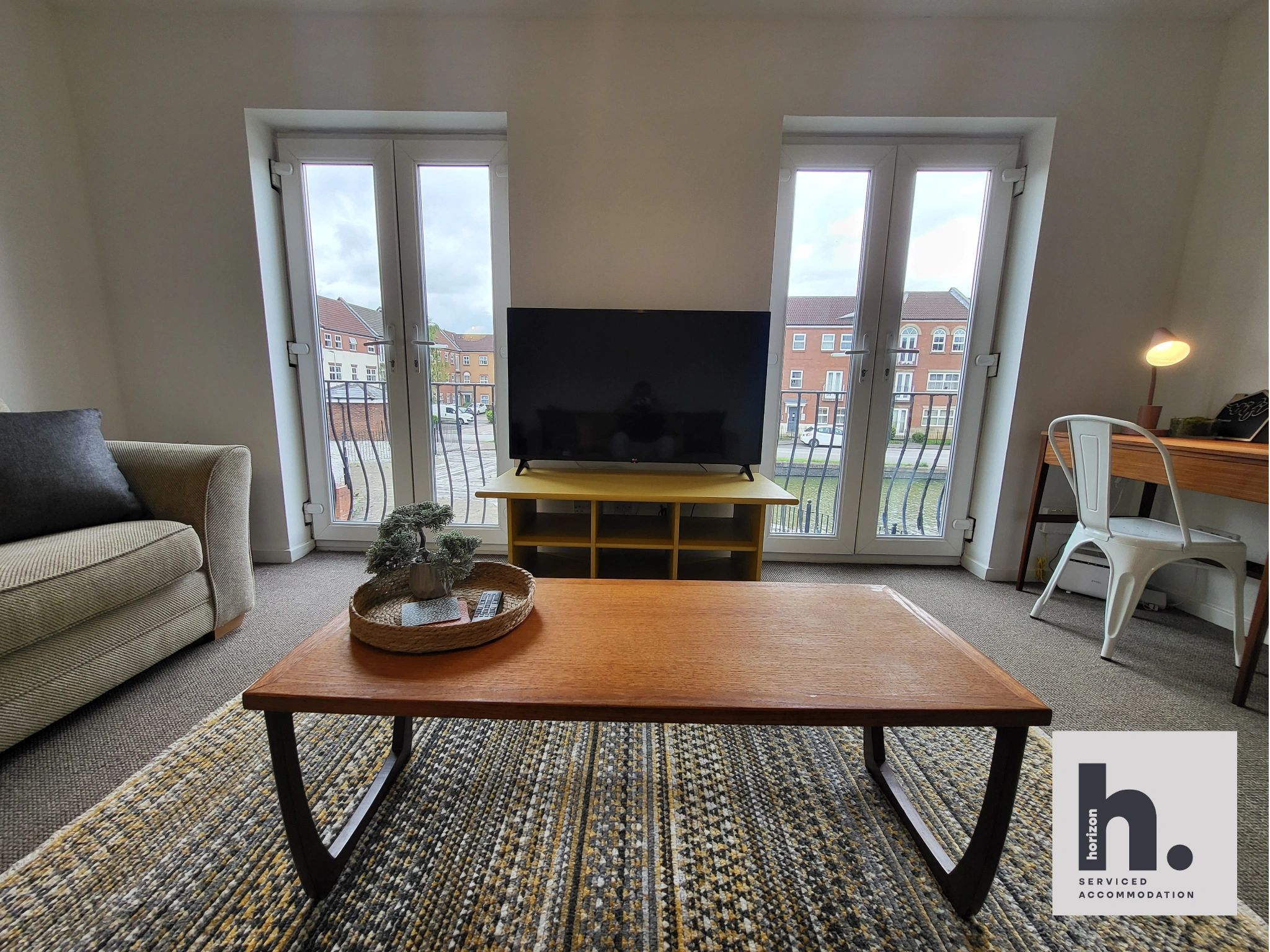 Modern living room with a TV, sofa, and cozy decor near large windows.