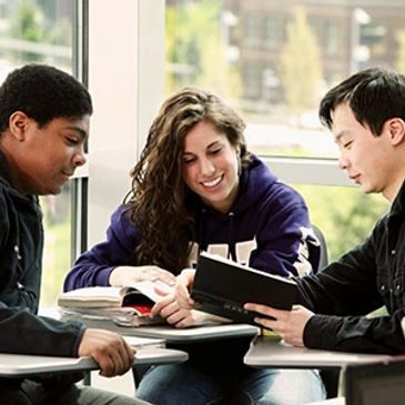 Three students studying together and smiling in a classroom.