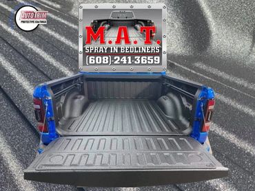 Blue truck bed with black spray-in bedliner coating, promoting M.A.T. Spray In Bedliners.