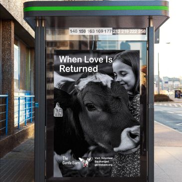 A girl affectionately hugs a cow at a bus stop ad.