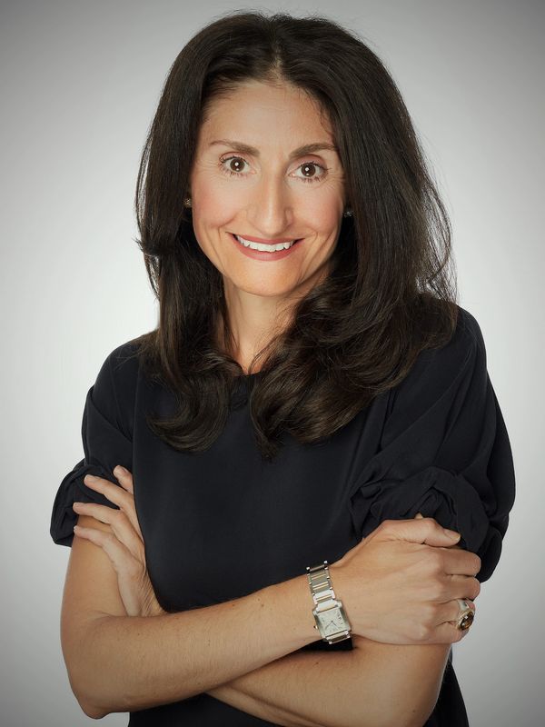 A smiling business woman standing in front of a camera with her arms crossed.