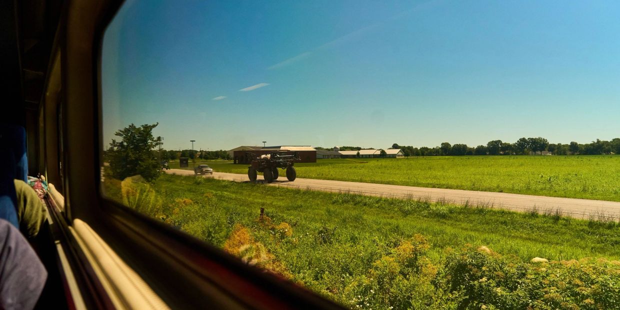train passenger view of a tractor driving down a road parallel to the train.