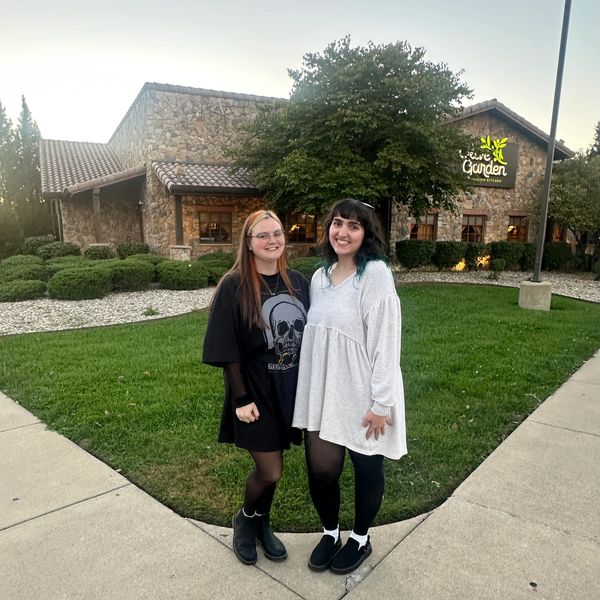 Two women smiling outside Olive Garden restaurant at dusk.