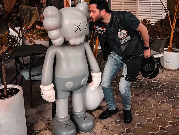 A man playfully kisses a large gray cartoon statue with crossed-out eyes.