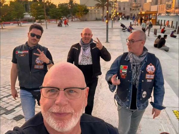 Four men walking outdoors at sunset, two making peace signs.