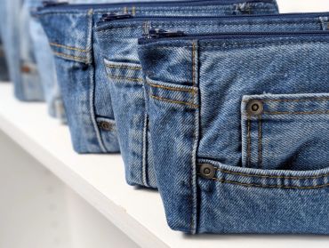 Row of folded blue jeans on a shelf.