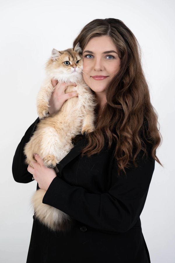 Woman with long brown hair holds a fluffy beige cat close to her face.