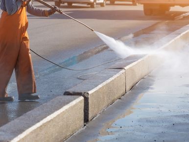 Worker cleaning driveway with gasoline high pressure washer splashing the dirt, asphalt road border.