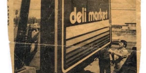 Vintage photo of a man installing a large deli market sign.