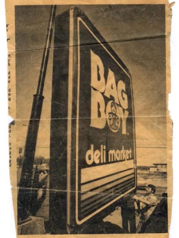 Vintage photo of a man installing a large deli market sign.