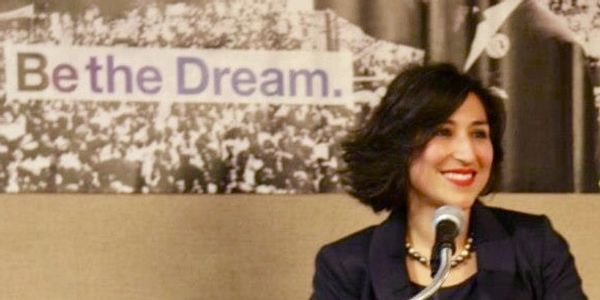 Dr Cio smiling in front of a microphone, with a banner behind saying "Be the Dream"