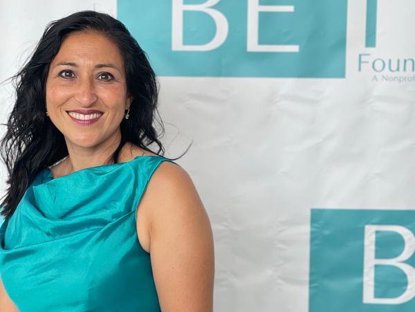 Dr Cio wearing a blue dress in front of a Be It banner.