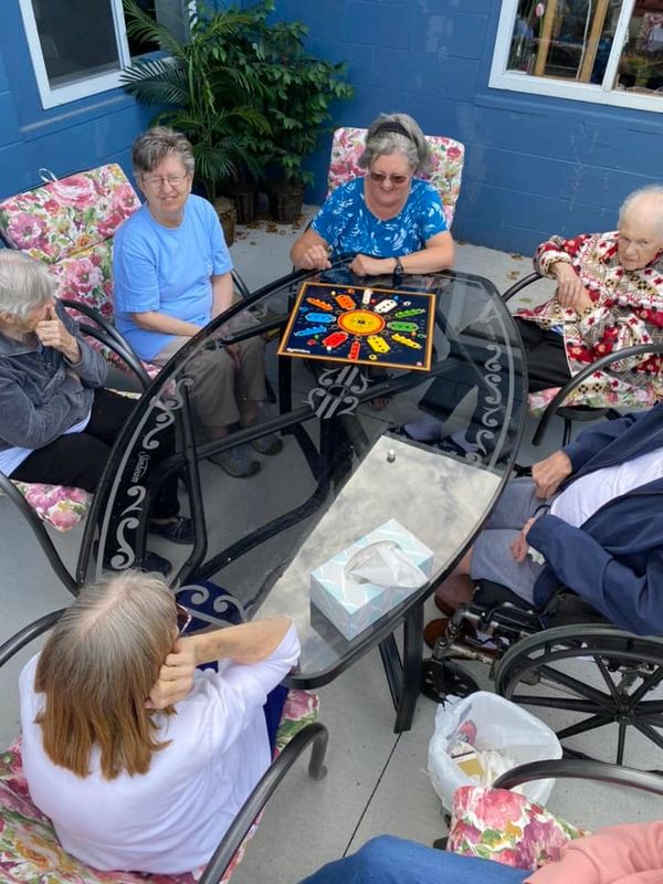 Elderly women gathered around a glass table playing a colorful board game outdoors.