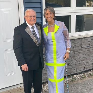 An elderly couple dressed elegantly, standing outside a house.