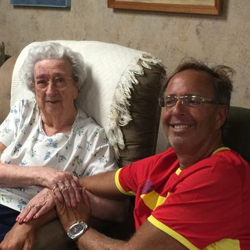 Elderly woman and man holding hands, smiling warmly indoors.