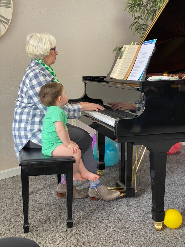 An elderly woman teaches a young child to play piano, sharing a tender moment.