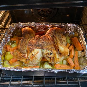 Roasted chicken with seasoned carrots and potatoes in an oven.