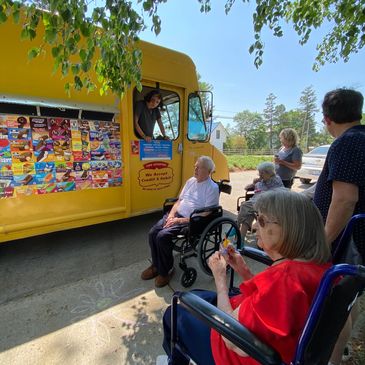 Elderly people in wheelchairs buying ice cream from a yellow truck.