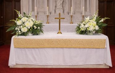 Church altar decorated with white flowers and a gold cross.