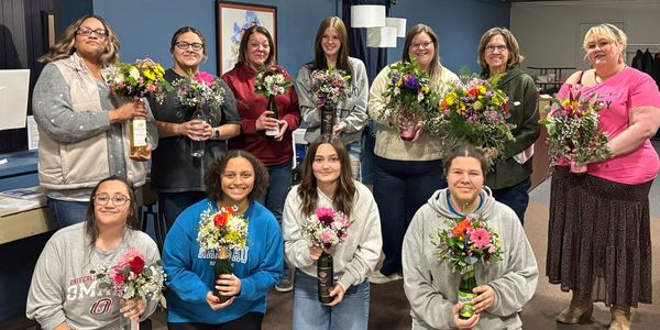 Group of smiling women holding colorful flower arrangements indoors.