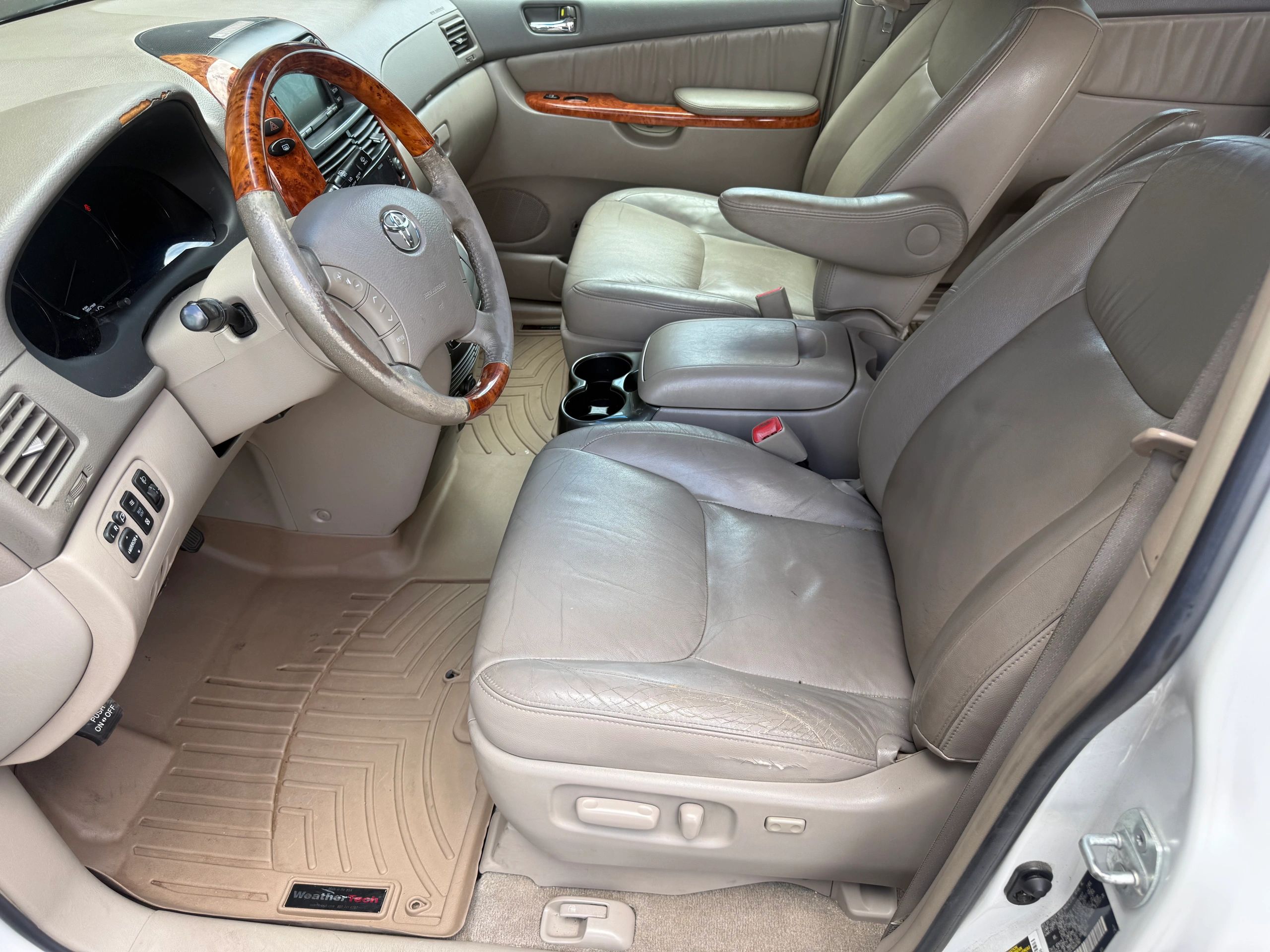 Interior of a beige leather Toyota car with wood accents and custom floor mats.