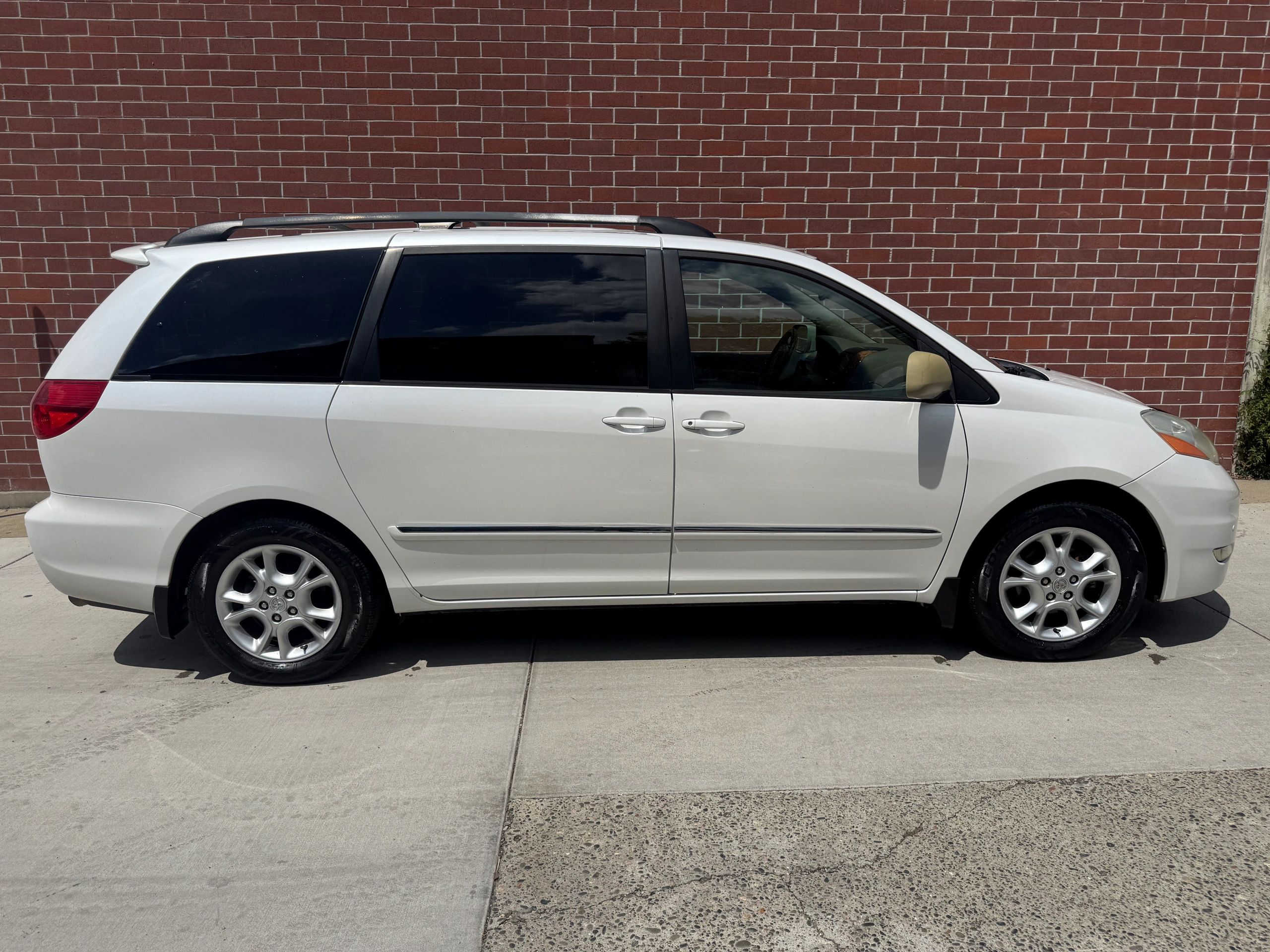 White minivan parked beside a red brick wall on a sunny day.