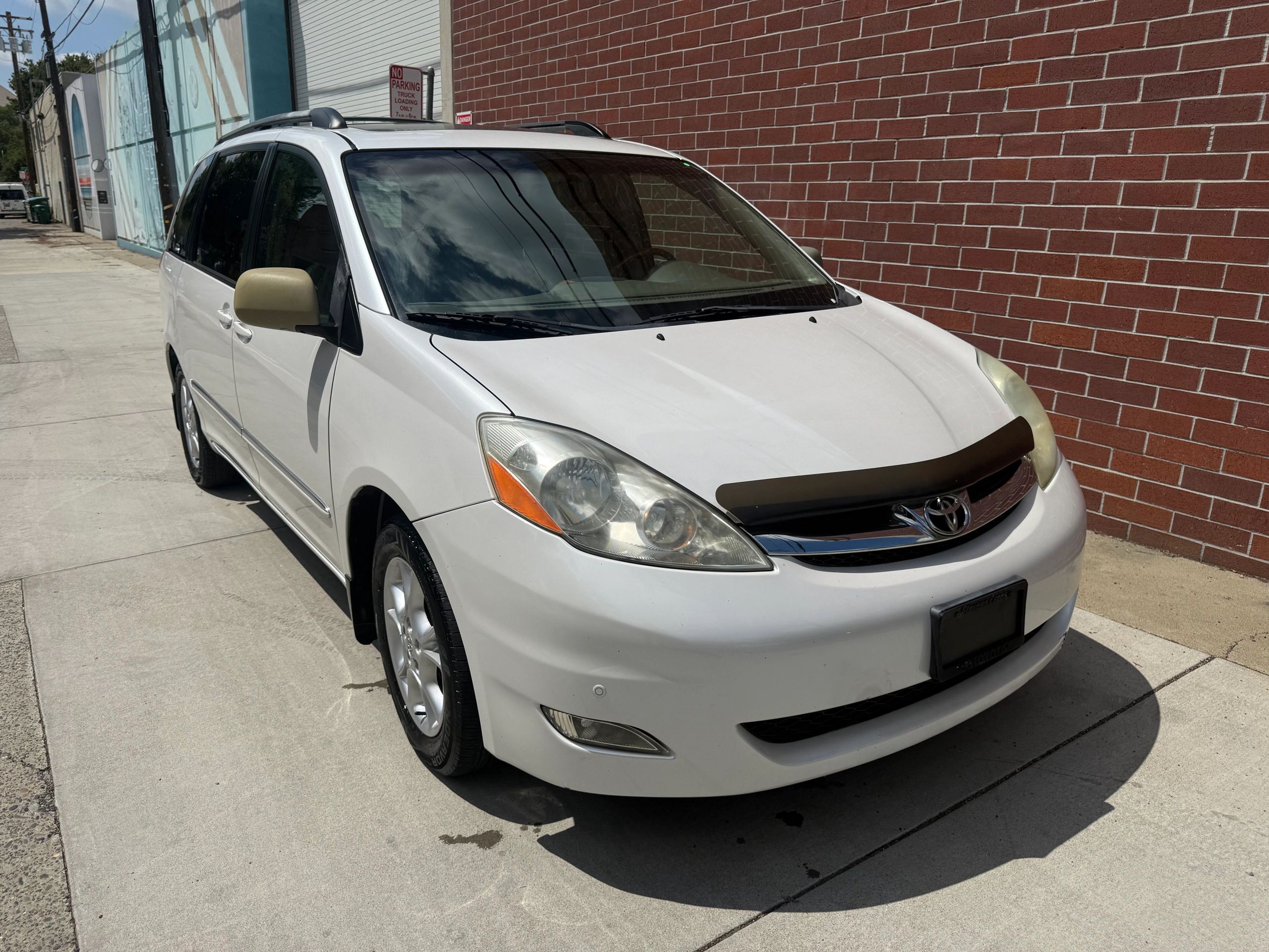 White Toyota minivan parked beside a brick wall on a sunny day.