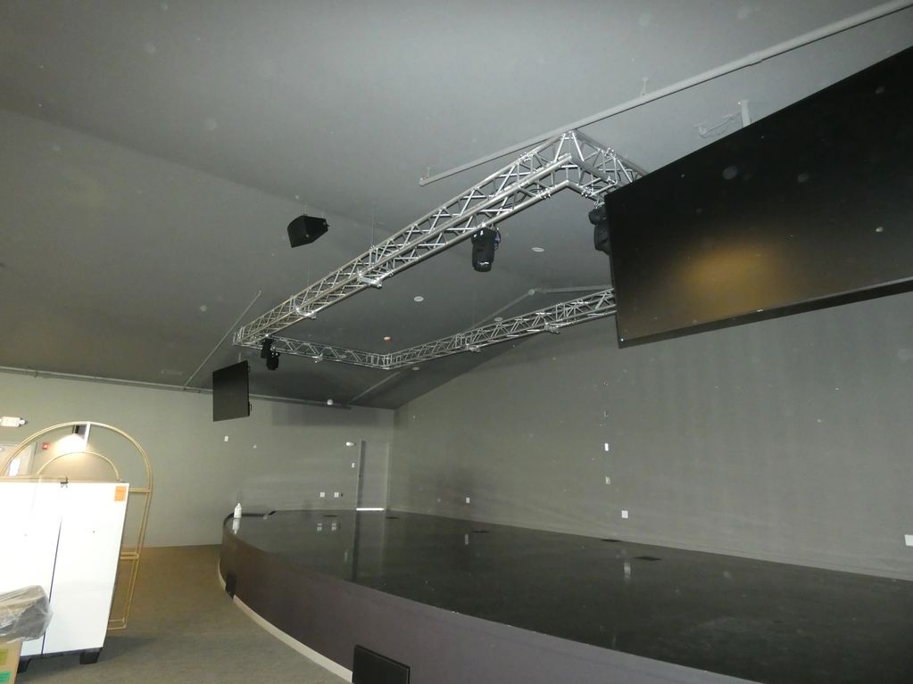 Empty stage with overhead lighting and large screens in a gray room.