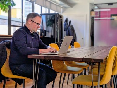Man working on laptop in a modern office with yellow chairs.