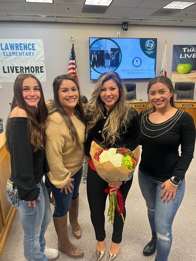 Four women smiling inside a meeting room, one holding a bouquet of flowers.
