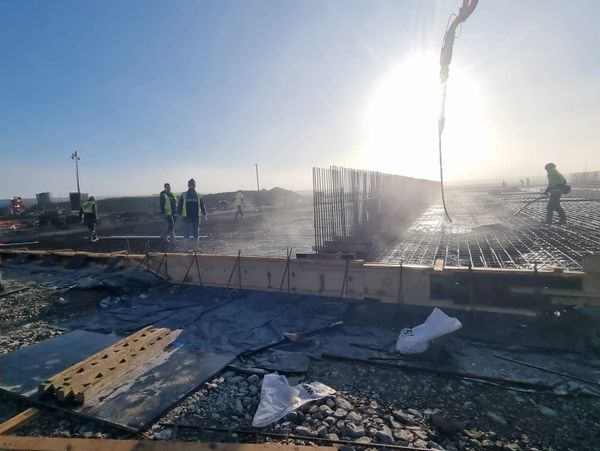 Construction workers pouring concrete on a large foundation under bright sunlight.