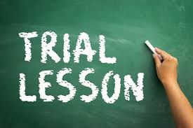 Hand writing 'TRIAL LESSON' on a chalkboard with white chalk.