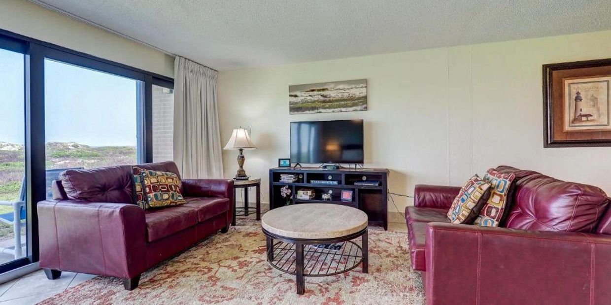 Cozy living room with two burgundy leather sofas, a round coffee table, and a TV on a stand.