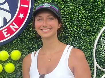 Smiling woman in a tennis-themed setting with tennis balls and racket.
