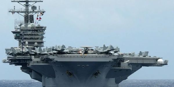 Front view of a large aircraft carrier at sea with planes on deck.