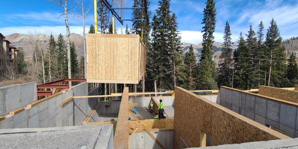Construction workers assembling wooden panels for a house frame in a forested mountain area.