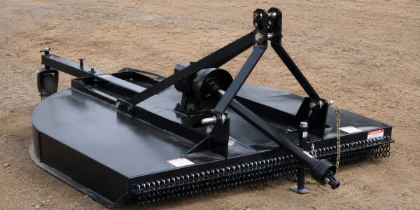 Black agricultural rotary cutter on dirt ground.