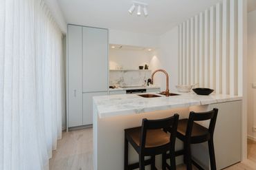 Modern kitchen with marble island and dark wooden chairs.