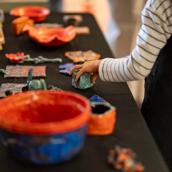 Child's hand exploring colorful ceramic art pieces on a black table.