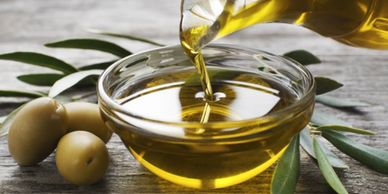 Olive oil being poured into a bowl with olives and leaves beside it.