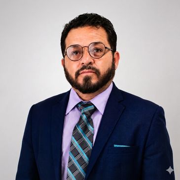 Man in a blue suit, purple shirt, and striped tie with glasses.